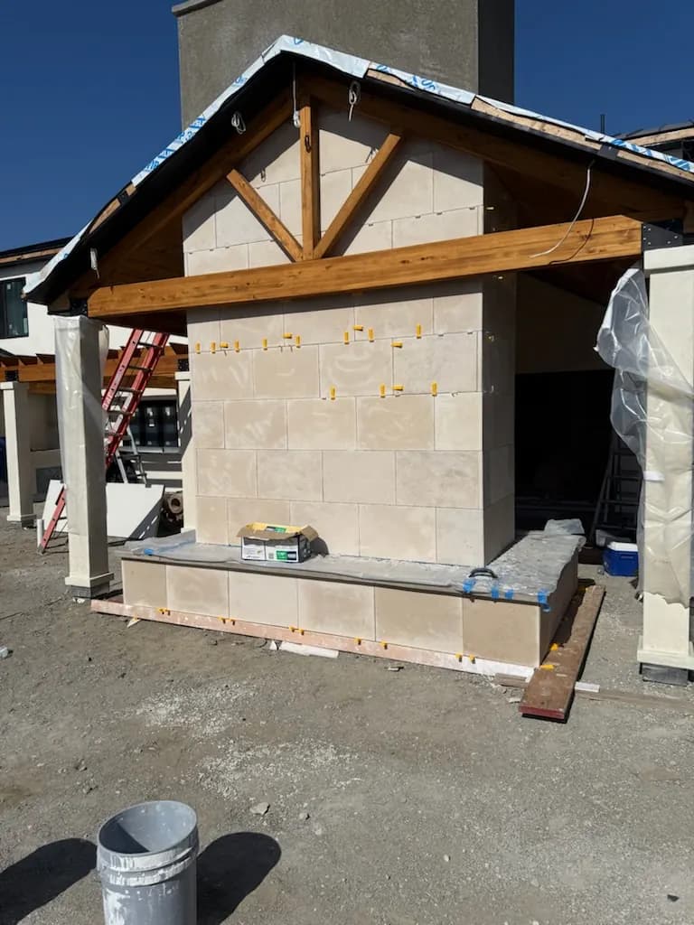 Outdoor stone fireplace under construction with a wood timber frame on a backyard patio