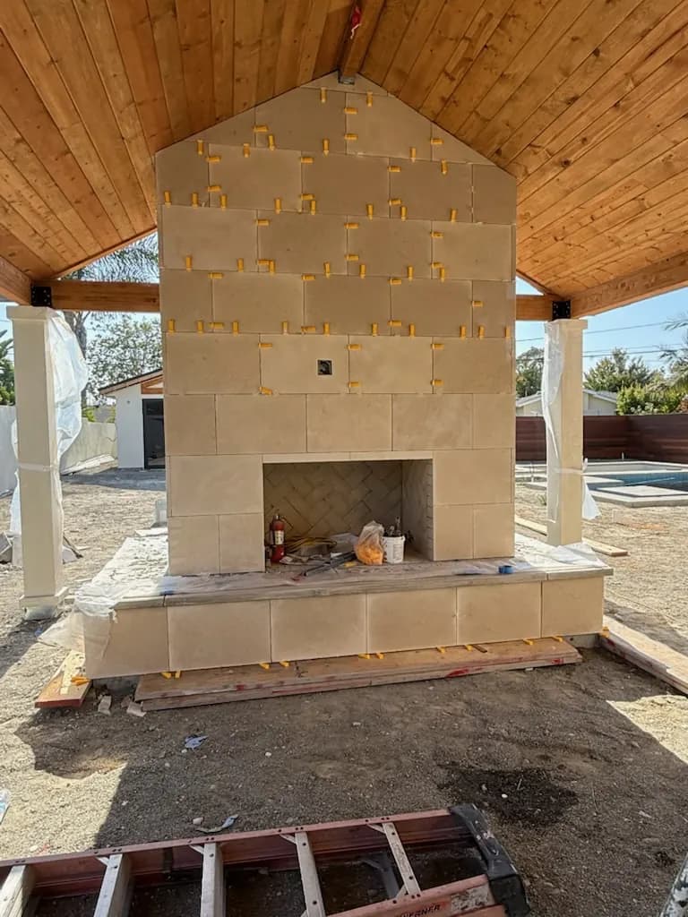 Outdoor stone fireplace with tile veneer taking shape under a covered patio