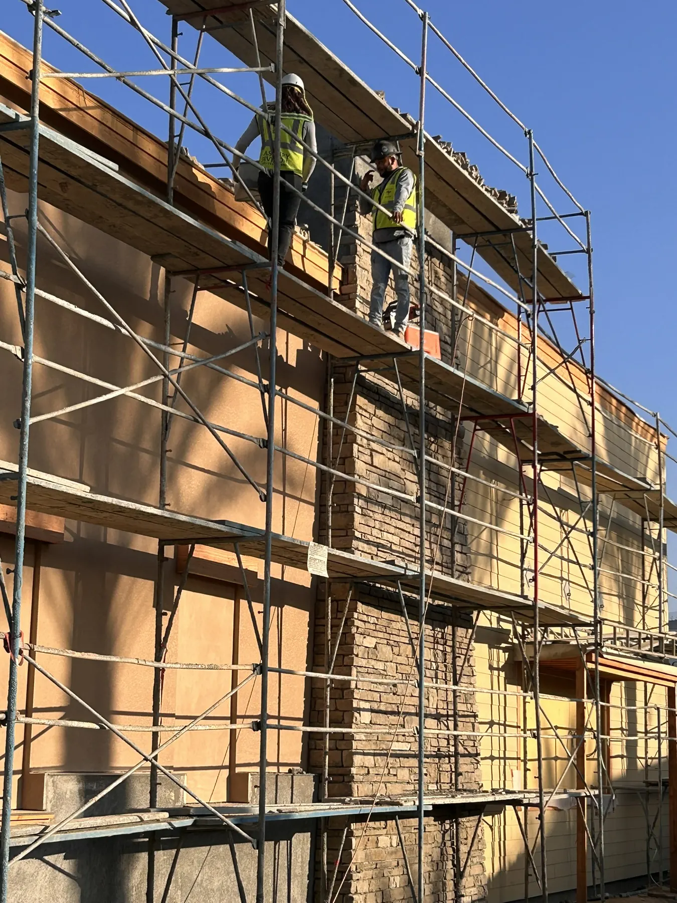 Masons on scaffolding installing stone veneer on a multi-story residential building