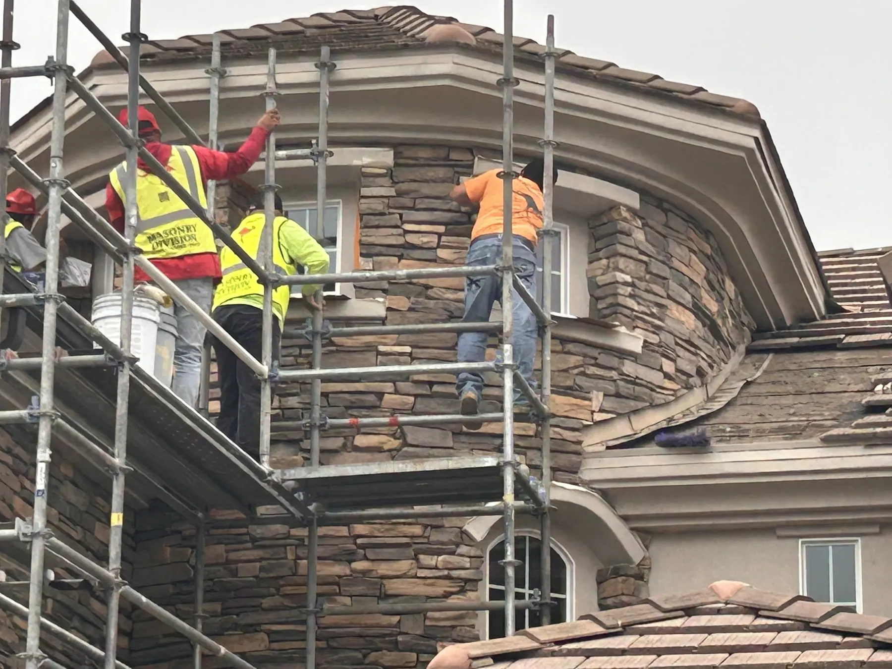 Masonry crew installing stone veneer around a turret window on a home exterior