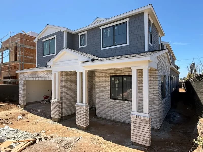 New home construction with brick veneer porch columns and gray shingle siding