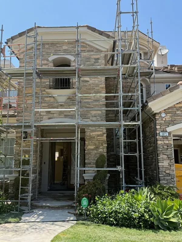 Scaffolding on a stone veneer home exterior with arched window details