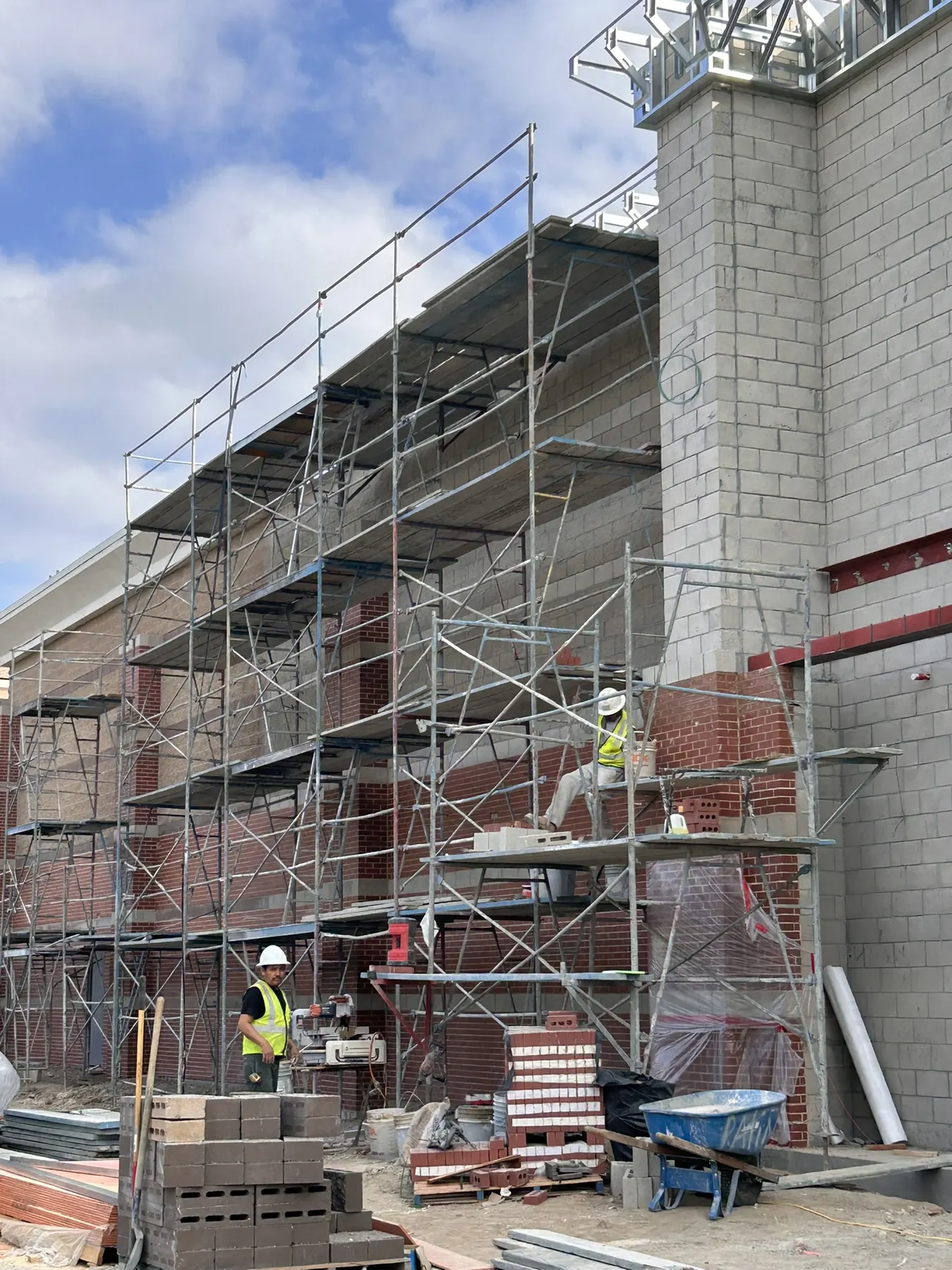 Masons on scaffolding installing brick veneer on a large block building