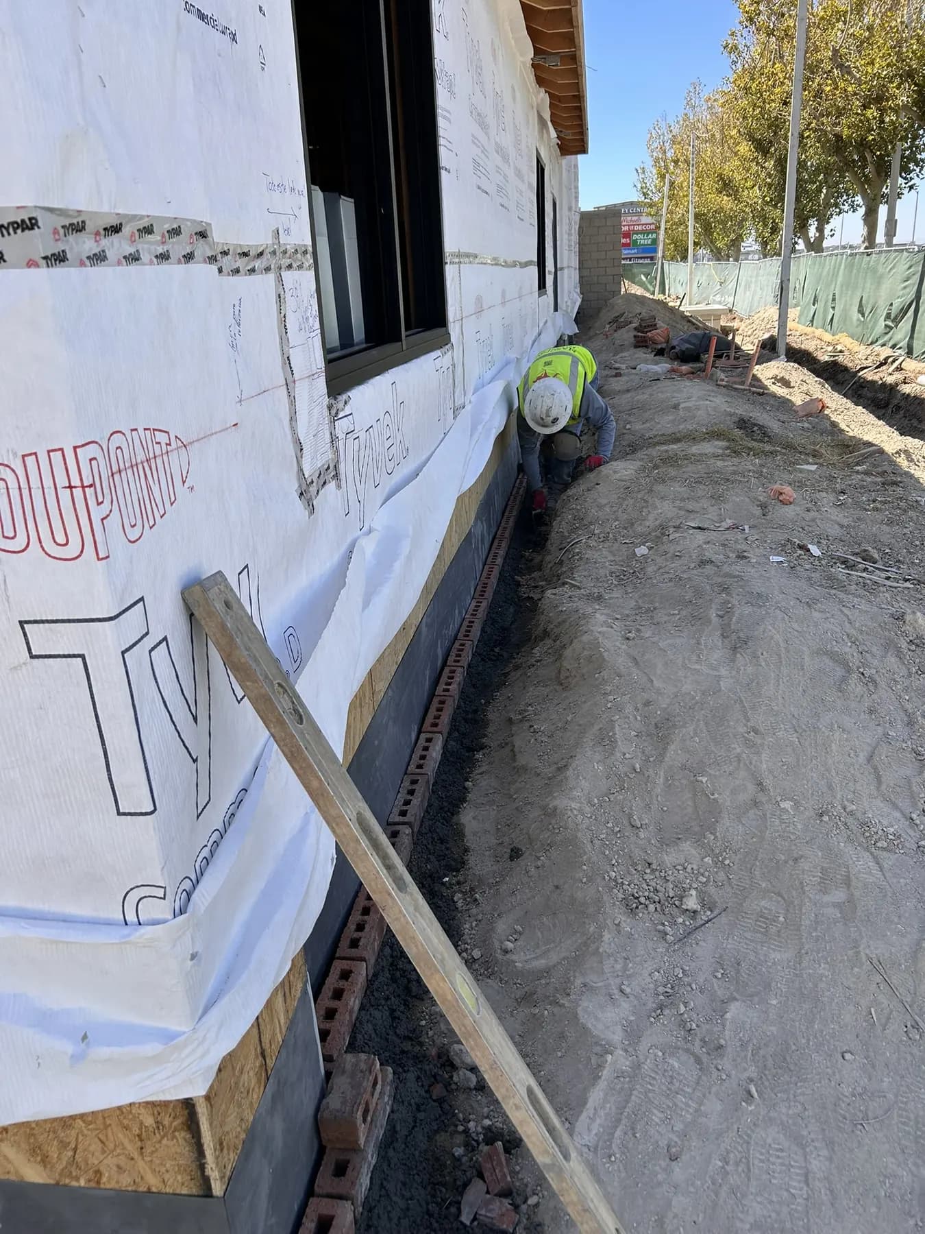 Mason leveling a brick foundation course along a home under construction
