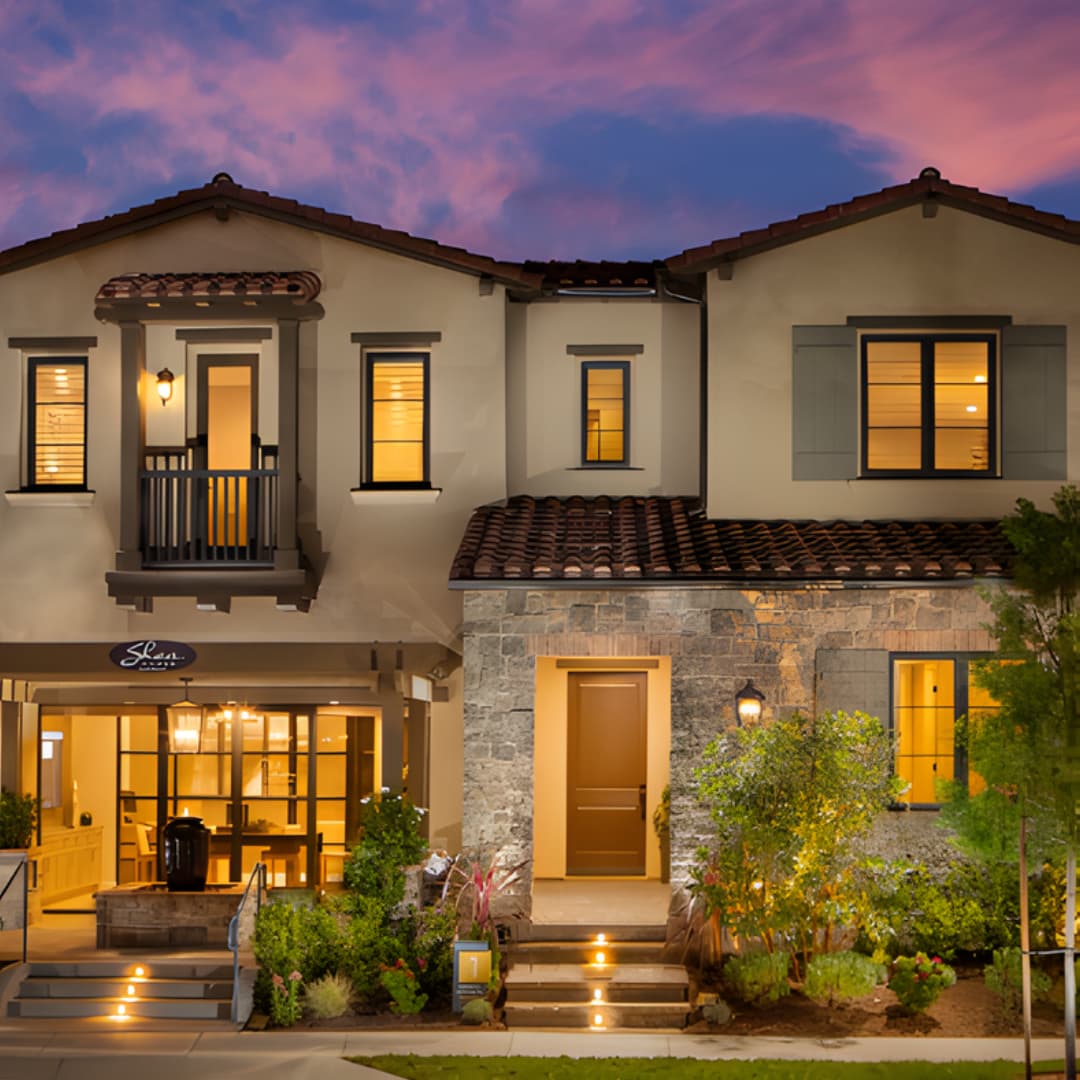 Two-story home with lit windows and landscaped front yard at dusk
